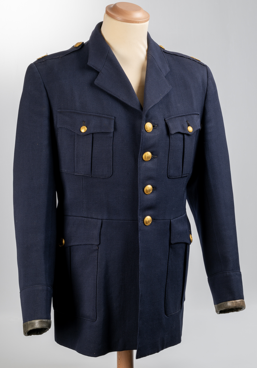 Uniformsjacka m/1954, för konstapel. Mörkblå med skinnskodda ärmslut. Knäpps med fyra knappar. Två bröstfickor- och två framfickor med lock och knapp. Två innerfickor. Sprund baktill med två knappar. Axelklaffar med uniformsknapp och emblem/lilla riksvapnet. Samtliga uniformsknappar i förgylld gulmetall, präglade med Växjö stadsvapen (år 1939-54), föreställande S:t Sigfrid.