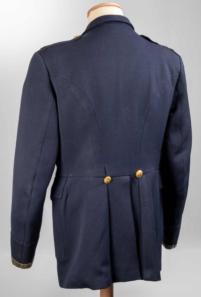 Uniformsjacka m/1954, för konstapel. Mörkblå med skinnskodda ärmslut. Knäpps med fyra knappar. Två bröstfickor- och två framfickor med lock och knapp. Två innerfickor. Sprund baktill med två knappar. Axelklaffar med uniformsknapp och emblem/lilla riksvapnet. Samtliga uniformsknappar i förgylld gulmetall, präglade med Växjö stadsvapen (år 1939-54), föreställande S:t Sigfrid.
