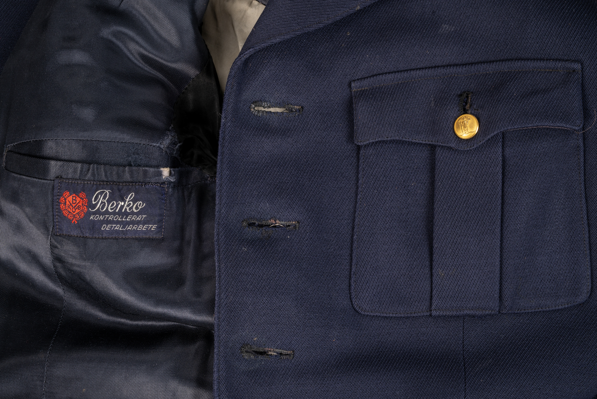 Uniformsjacka m/1954, för konstapel. Mörkblå med skinnskodda ärmslut. Knäpps med fyra knappar. Två bröstfickor- och två framfickor med lock och knapp. Två innerfickor. Sprund baktill med två knappar. Axelklaffar med uniformsknapp och emblem/lilla riksvapnet. Samtliga uniformsknappar i förgylld gulmetall, präglade med Växjö stadsvapen (år 1939-54), föreställande S:t Sigfrid.