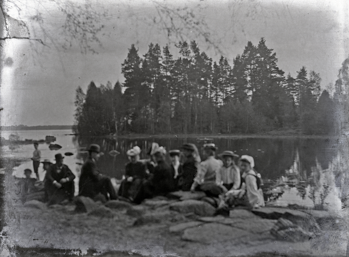 Ett sällskap har slagit sig ner på några berghällar invid en sjö.
Suddigt foto.