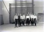 En mindre skolklass, uppställda i en gymnastiksal, klädda för gymnastik.