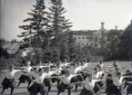 En trupp kvinnliga gymnaster övar i det fria utanför dåv. seminariet, dvs numera Ringsbergsskolan i Växjö.  I bakgrunden syns skolans växthus och  dåv. cellfängelset.