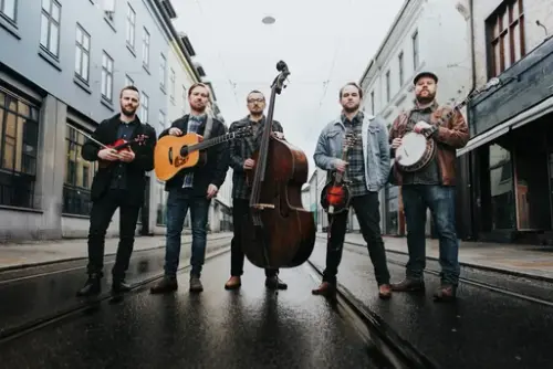 Fem menn står midt i en bygate med sine instrumenter. 