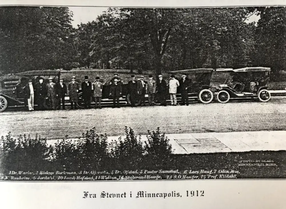 Historisk bilde av en rekke menn med hatt som står foran fire biler.