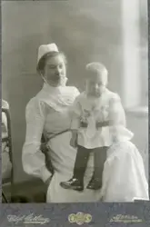 Porträtt av Amanda Palm i sjuksköterskedräkt med ett barn i 