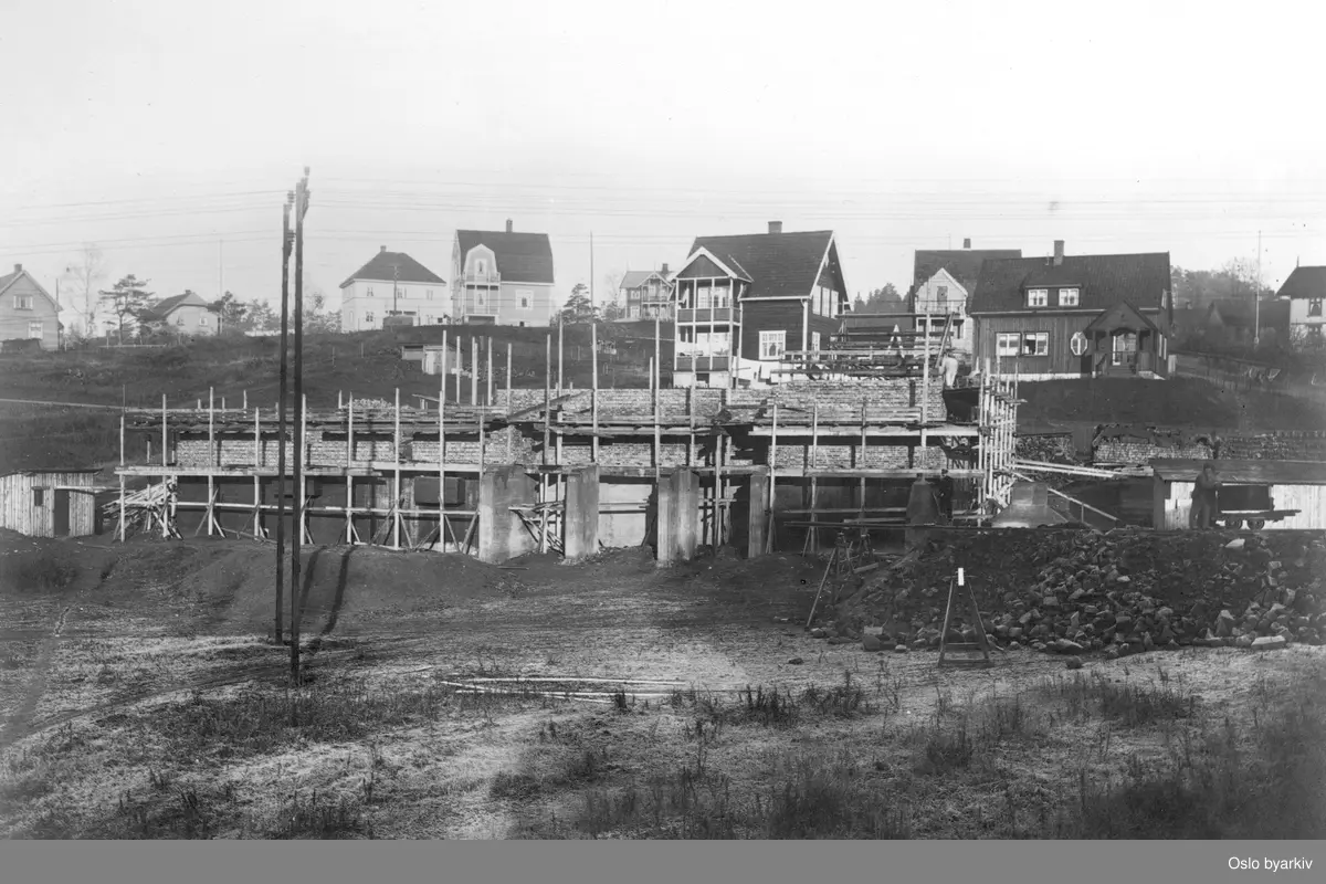 Bildet tatt i forbindelse med utbyggingen av Lilleakerbanen som ble åpnet i 1919, reisverk til stasjonsbygning på Lilleaker, villabebyggelse bak