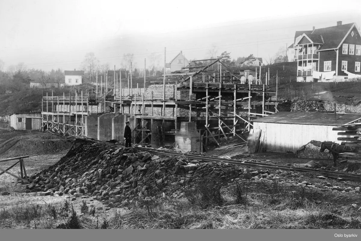 Bildet tatt i forbindelse med utbyggingen av Lilleakerbanen som ble åpnet i 1919, reisverk til stasjonsbygning på Lilleaker, villabebyggelse bak.