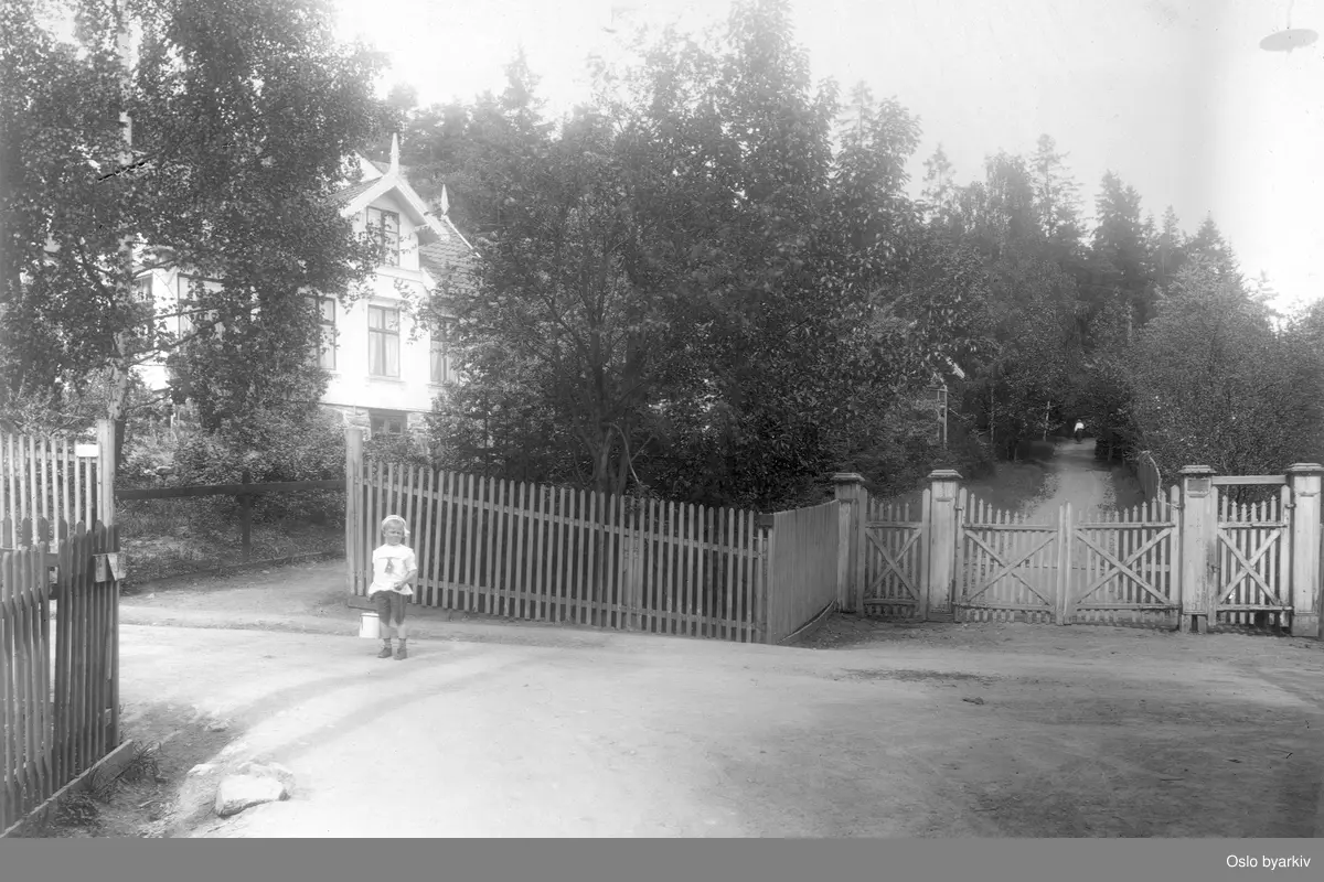 Barn foran inngjerdet sveitservilla i hage. Bildet er tatt i forbindelse med utbyggingen av Lilleakerbanen.