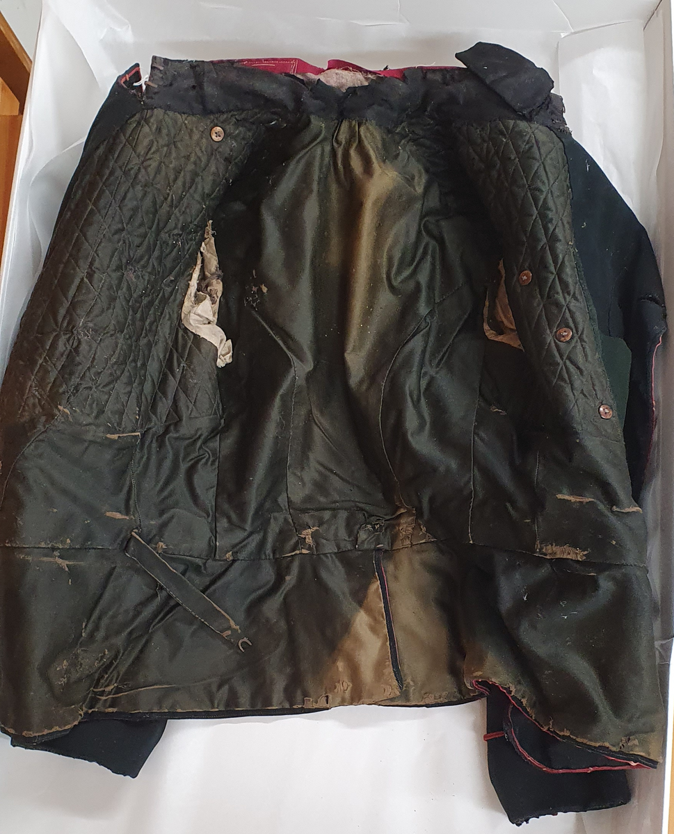 Svart jakke fra det norske forsvaret. Det går en rød stripe langs ermene og nedover jakkeåpningen. Jakken har to rader med knapper på framsiden som går opp til kragen. Kragen er rød, med to hvite tykke striper. Det er tre knapper på i hver ende av ermene. Knappene er sølvfargede, med dekorative horn. Innsiden av jakken er trekt med silkelignende tekstil. Jakken er lappet øverst på høyre erme.