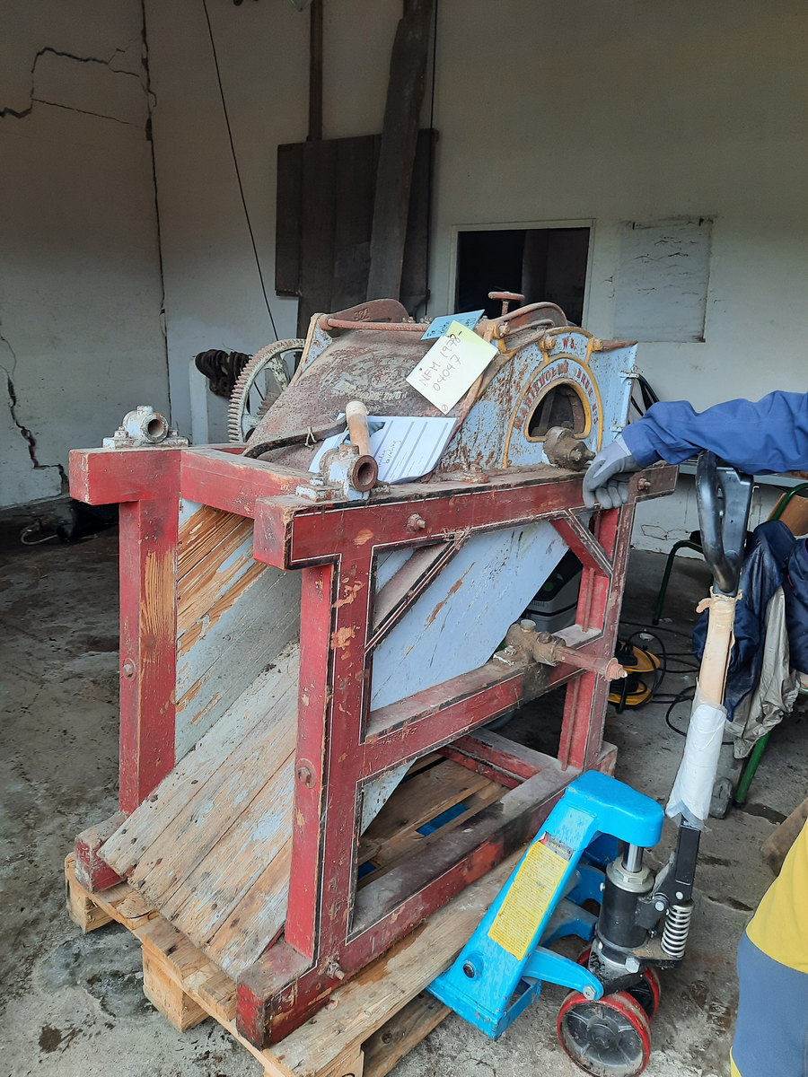 Piggtreskemaskin. Kontruksjon (stativ) i tre rundt maskina. 
Øvste del av maskina er i metall, medan nedste (renne) er i tre. Maskina har opning oppe på eine kortsida, der det er monternt ein metall sylinder med piggar (på aksling). Under metall sylindaren er det ei trerenne som skrånar nedover. 
På eine sida av stativet er det montert fleire tannhjul som grip i kvarandre. Stort hjul i tre ytst. Feste for sveiv stikk ut på andre sida. 
Sveiva driv hjulet via aksling under tre-renna, og via tannhjule vil den pigga metallsylinderen dreie rundt.
Treråma er raudlilla med kvit og svart stripe. Maskina er turkis med gule kantar og raud skrift på sidene.