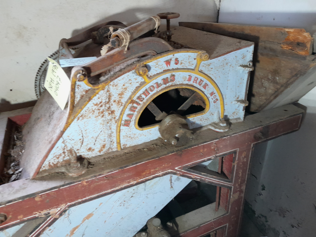 Piggtreskemaskin. Kontruksjon (stativ) i tre rundt maskina. 
Øvste del av maskina er i metall, medan nedste (renne) er i tre. Maskina har opning oppe på eine kortsida, der det er monternt ein metall sylinder med piggar (på aksling). Under metall sylindaren er det ei trerenne som skrånar nedover. 
På eine sida av stativet er det montert fleire tannhjul som grip i kvarandre. Stort hjul i tre ytst. Feste for sveiv stikk ut på andre sida. 
Sveiva driv hjulet via aksling under tre-renna, og via tannhjule vil den pigga metallsylinderen dreie rundt.
Treråma er raudlilla med kvit og svart stripe. Maskina er turkis med gule kantar og raud skrift på sidene.