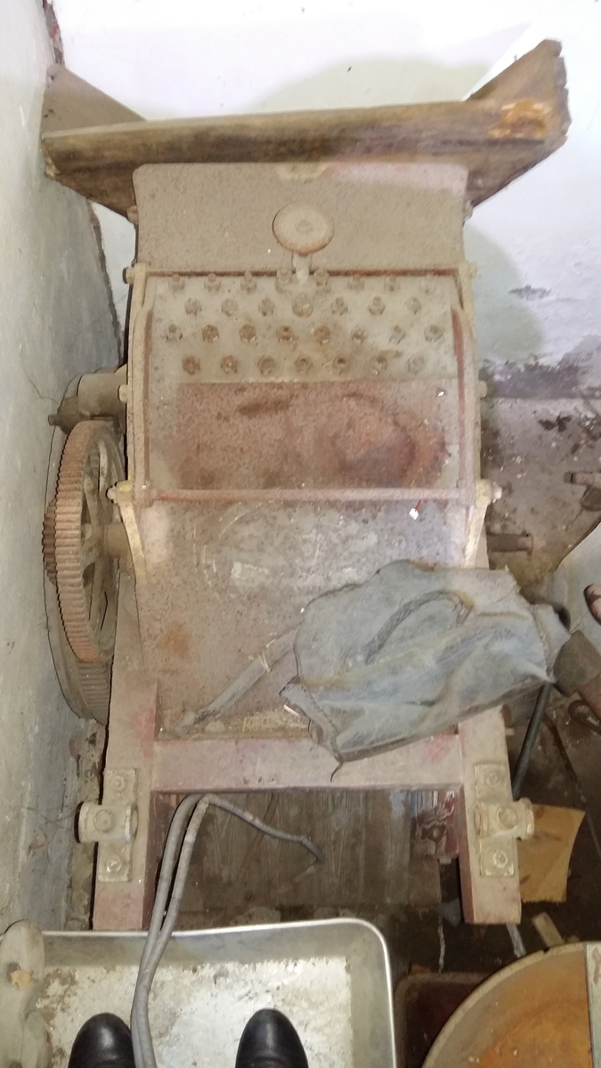 Piggtreskemaskin. Kontruksjon (stativ) i tre rundt maskina. 
Øvste del av maskina er i metall, medan nedste (renne) er i tre. Maskina har opning oppe på eine kortsida, der det er monternt ein metall sylinder med piggar (på aksling). Under metall sylindaren er det ei trerenne som skrånar nedover. 
På eine sida av stativet er det montert fleire tannhjul som grip i kvarandre. Stort hjul i tre ytst. Feste for sveiv stikk ut på andre sida. 
Sveiva driv hjulet via aksling under tre-renna, og via tannhjule vil den pigga metallsylinderen dreie rundt.
Treråma er raudlilla med kvit og svart stripe. Maskina er turkis med gule kantar og raud skrift på sidene.