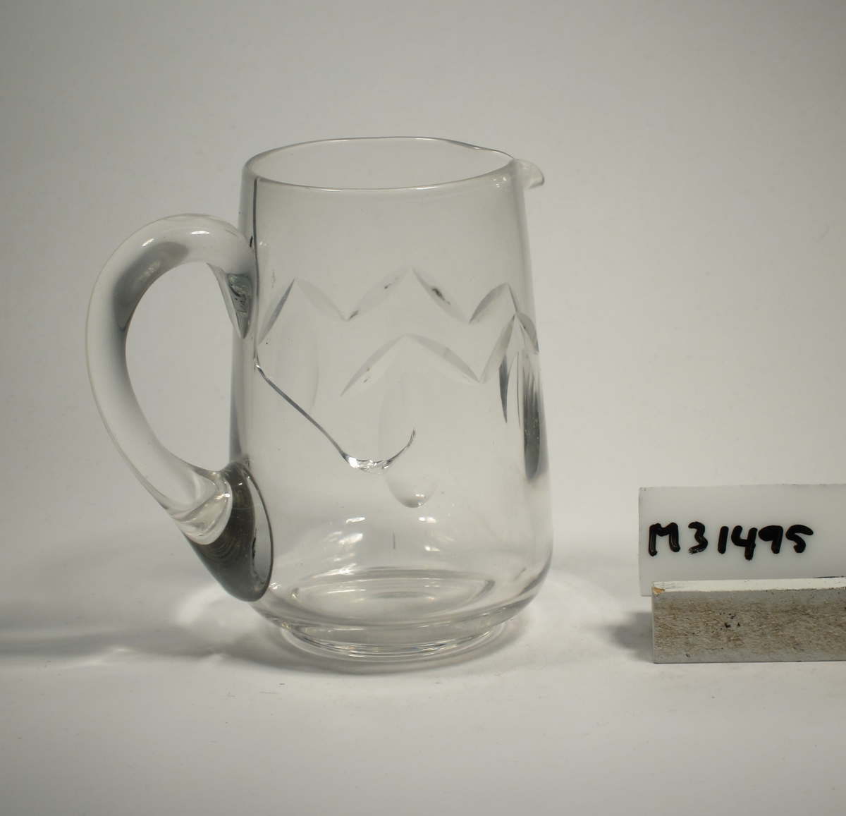 Konande form, avrundad mot botten. Enkelt skär- och olivslipat mönster runt kupan. Påklippt grepe.