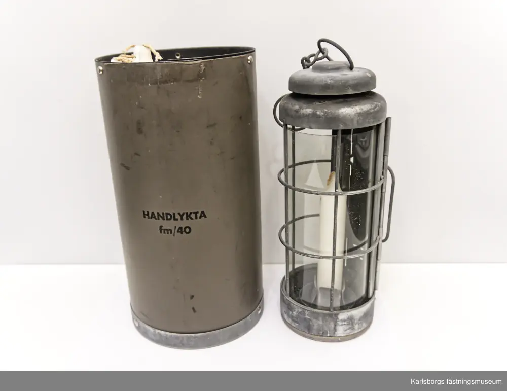 Handlykta fm/1940 för stearinljus med behållare vars lock saknas. Behållaren har fack, av metallskiva, för fyra stycken stearinljus. Själva lyktan består av metall och celluloidskiva. Celluloidskivan kan bytas ut mot en annan.