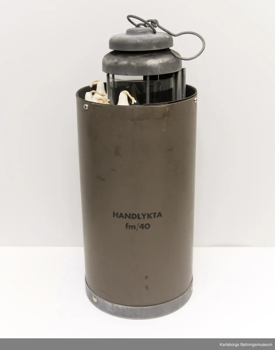 Handlykta fm/1940 för stearinljus med behållare vars lock saknas. Behållaren har fack, av metallskiva, för fyra stycken stearinljus. Själva lyktan består av metall och celluloidskiva. Celluloidskivan kan bytas ut mot en annan.