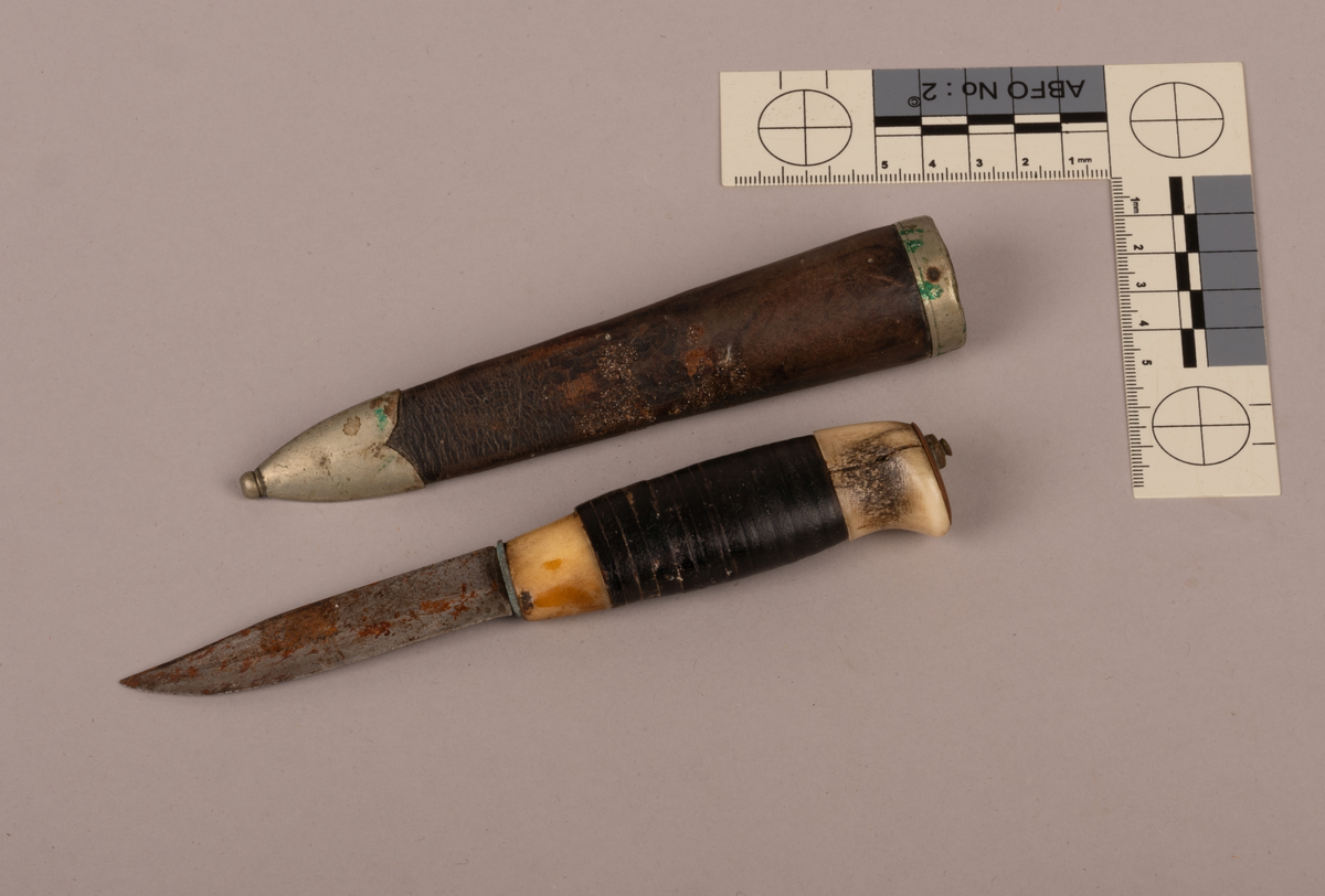 Kniv og slire. Kniven har skaft i bein som er slipt glatt. Rundt skaftet er det trukket skinn. Skinnet er surret rundt skaftet. Sliren består av metall (sølv) og skinn. På skinnet vises konturer av tidligere dekoreringsarbeid. Sømmen bak sliren er meget tett, bein og jevnt sydd. På slirens inngangsparti er det lagd et sølvbeslag som fungerer som en slags falsavslutning. Denne har dekor i form av to streker som går parallelet med lengdretningen av beslaget, altså på tvers av sliren. Den ene streken er nesten slitt bort. 
I tuppen av sliren er det festet et beslag av metall eller sølv. Dette er avsluttet med en liten kule, som utgjør tuppen av sliren.  Kniv og slire er forseggjort og er et pent arbeid.