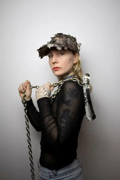  Konstnären Erika Kristoffersson Bredberg iförd keps håller i ett konstverk av glas med en kedja