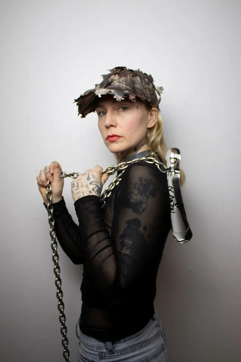  Konstnären Erika Kristoffersson Bredberg iförd keps håller i ett konstverk av glas med en kedja