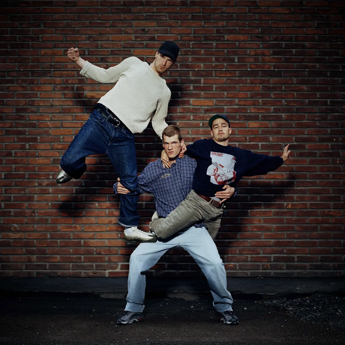 Tre menn i akrobatisk utøvelse foran murvegg