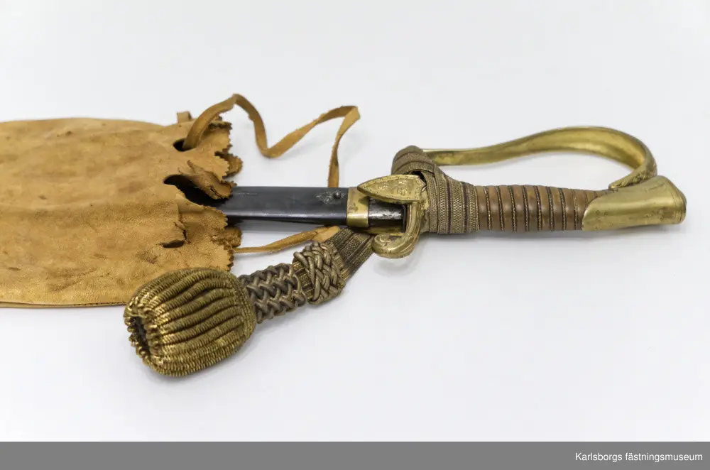 Sabel m/1889 (pallasch), tveeggad klinga med skålslipning på en längd av 71 cm. Total längd: 95cm. Klingans längd: 80cm. Klingans bredd: 3cm. Den yttre styrskenan är ciselerad i form av en sköld prydd med tre kronor. Baljan är av stål. Portepé m/1797, sabelhandrem i silke, medföljer.