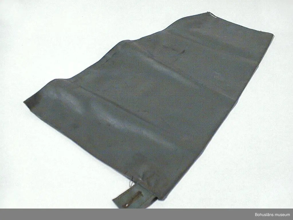 Grön avlång ärm. Upptill är det en grön stropp med ett knapphål.  Att dra utanpå skjorta som skydd för väta.
Denna typ av mudd såldes av Torvald Strannes skeppshandel på Smögen.

Övrig historik; se UM026422