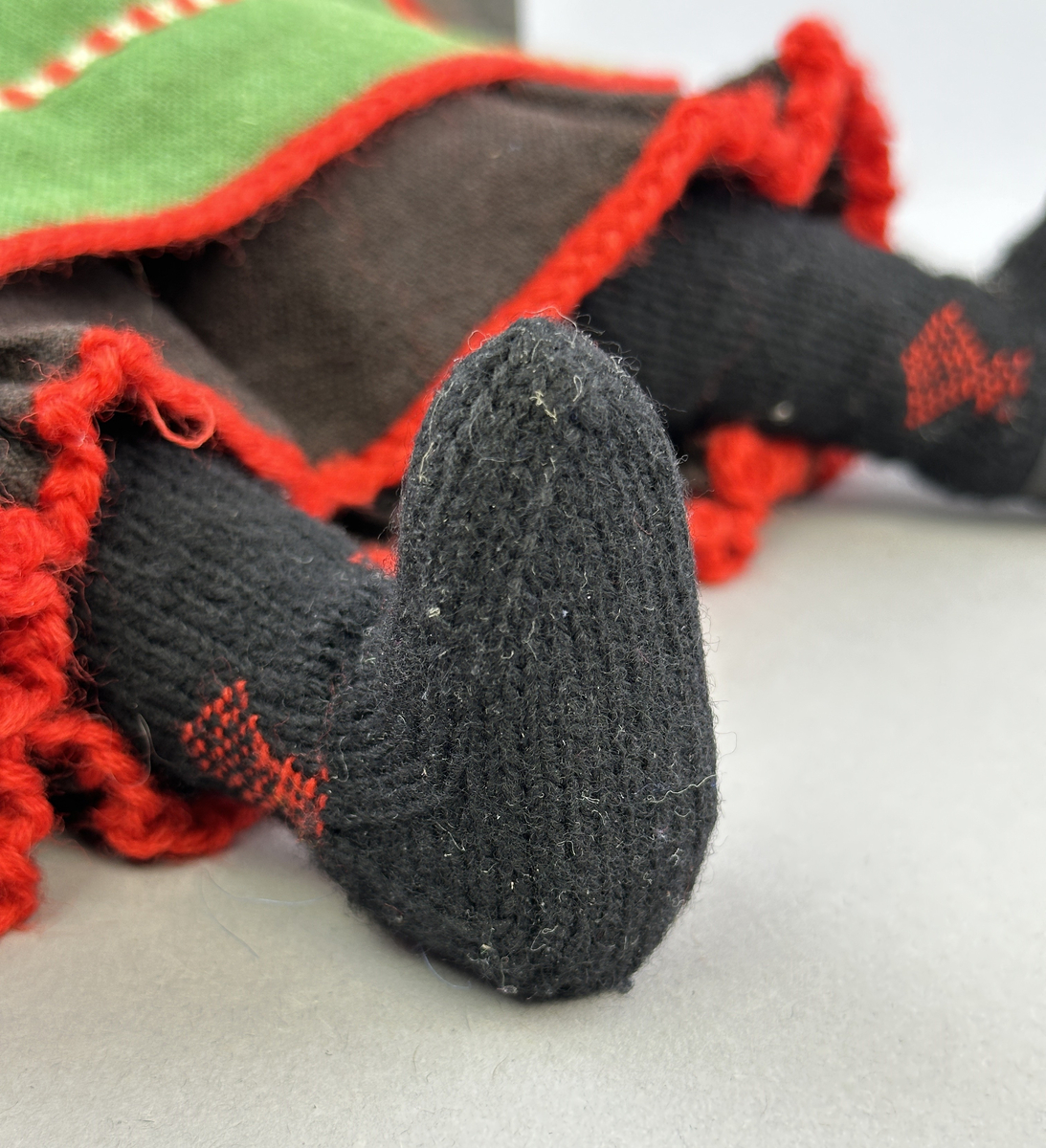 Docka klädd i kvinnlig sockendräkt från Norra Ny i Värmland. Kroppen är sydd i linnetyg och stoppad med textilt material. Huvud och händer är av lergods. Kläder sydda av handvävda tyger förutom skjorta, underkjol och halskläde, som är maskinvävt. Halskläde är broderat med tambursöm, skjortan med plattsöm och myrgång samt har stripade veck runt halskrage och manschetter. Även kjolen har lagda veck runtom och är fastsytt med livstycket. Förklädet, med 3 lagda veck på var sida, är kantad runtom med en tre-fläta gjord av rött ullgarn, vilket också kjolen har i nederkanten. Ullstrumporna är handstickade i slätstickning med en kant upptill i 2-2 resår och broderad med förstygn av rött ullgarn. Huvudet är prytt med hår av lintågor, som delvis är flätat till hårflätor samt ett målat hårnäver. Dockans fötter bär svarta skinnskor.