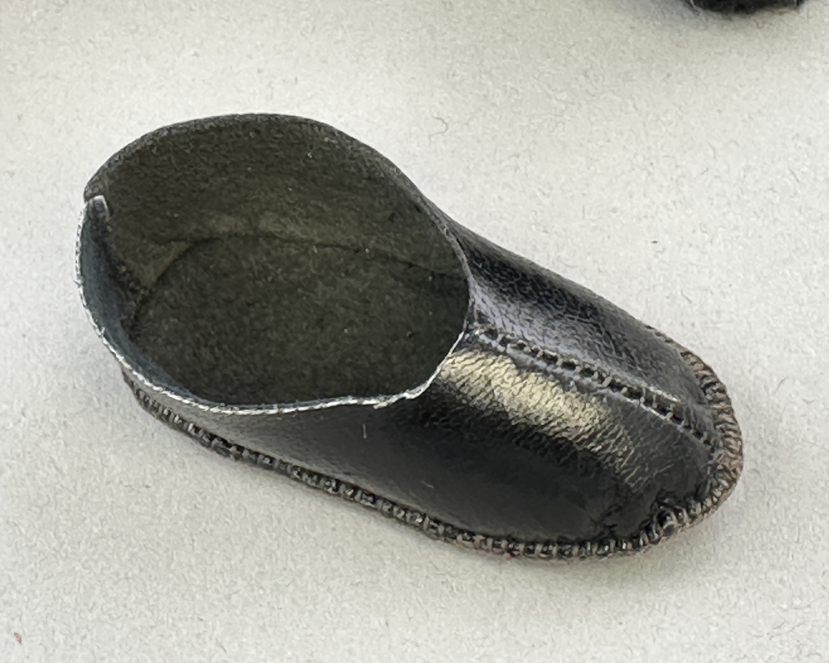 Docka klädd i kvinnlig sockendräkt från Norra Ny i Värmland. Kroppen är sydd i linnetyg och stoppad med textilt material. Huvud och händer är av lergods. Kläder sydda av handvävda tyger förutom skjorta, underkjol och halskläde, som är maskinvävt. Halskläde är broderat med tambursöm, skjortan med plattsöm och myrgång samt har stripade veck runt halskrage och manschetter. Även kjolen har lagda veck runtom och är fastsytt med livstycket. Förklädet, med 3 lagda veck på var sida, är kantad runtom med en tre-fläta gjord av rött ullgarn, vilket också kjolen har i nederkanten. Ullstrumporna är handstickade i slätstickning med en kant upptill i 2-2 resår och broderad med förstygn av rött ullgarn. Huvudet är prytt med hår av lintågor, som delvis är flätat till hårflätor samt ett målat hårnäver. Dockans fötter bär svarta skinnskor.