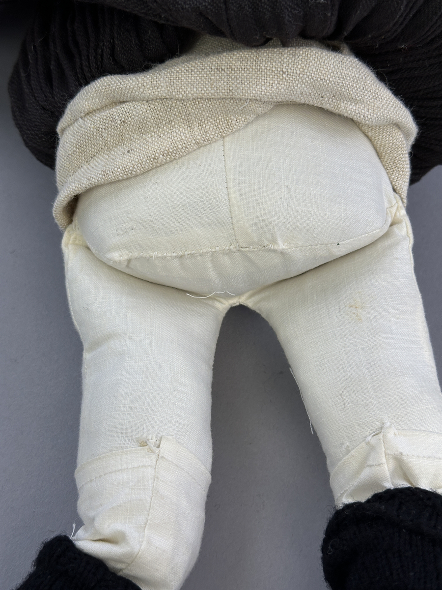 Docka klädd i kvinnlig sockendräkt från Norra Ny i Värmland. Kroppen är sydd i linnetyg och stoppad med textilt material. Huvud och händer är av lergods. Kläder sydda av handvävda tyger förutom skjorta, underkjol och halskläde, som är maskinvävt. Halskläde är broderat med tambursöm, skjortan med plattsöm och myrgång samt har stripade veck runt halskrage och manschetter. Även kjolen har lagda veck runtom och är fastsytt med livstycket. Förklädet, med 3 lagda veck på var sida, är kantad runtom med en tre-fläta gjord av rött ullgarn, vilket också kjolen har i nederkanten. Ullstrumporna är handstickade i slätstickning med en kant upptill i 2-2 resår och broderad med förstygn av rött ullgarn. Huvudet är prytt med hår av lintågor, som delvis är flätat till hårflätor samt ett målat hårnäver. Dockans fötter bär svarta skinnskor.