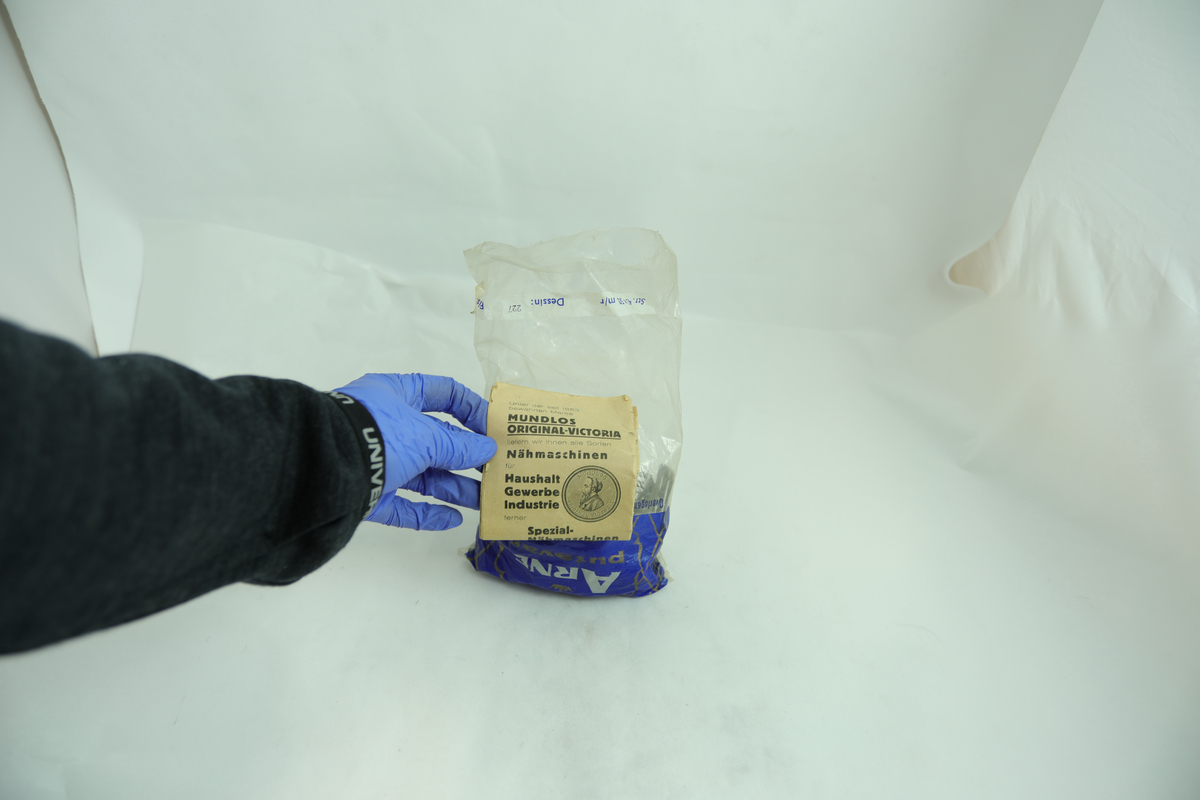 Plastpose med metalldeler og papirhefte til Mundlos symaskin.