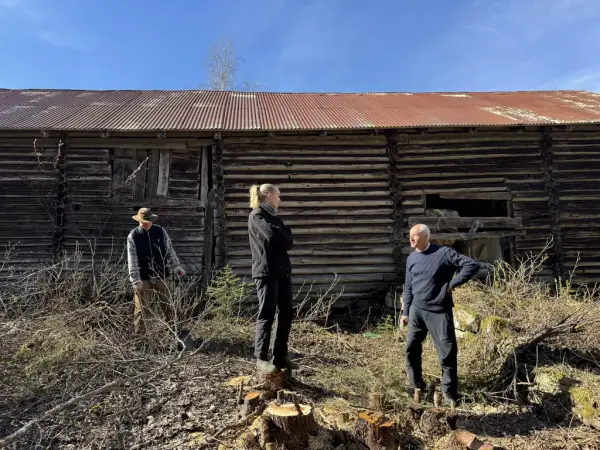 Tre personar framfor ein gamal tømmerlåve