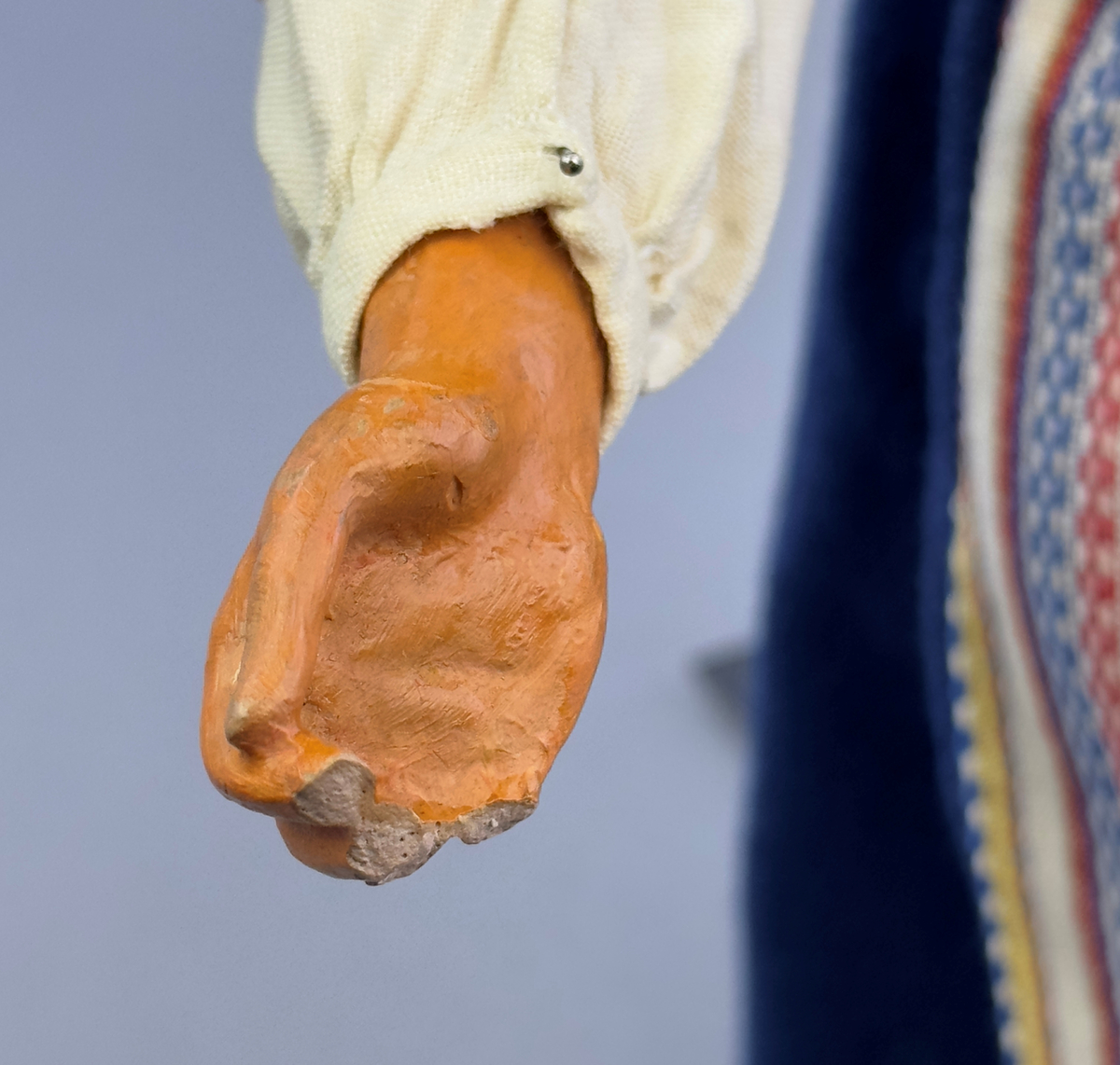 Docka klädd i kvinnlig sockendräkt från Ulleruds socken i Värmland. Kroppen är handsydd i linnetyg och stoppad med textilt material. Huvud och händer är av lergods. Kläder handsydda av handvävda tyger förutom skjorta, underkjol och halskläde, som är maskinvävt. Skjorta, broderad med myrgång runt sprund, har halsspjäll, halslinning och handlinning. Halsklädet, med tryck i gult, rosa och beige, hålls ihop av en sölja i nysilver med graverat mönster. Kjol sydd med lagda veck runtom, utom under förkläde, vars linning består av ett bomullsband. Förkläde, vävt i tuskaft och munkabälte, har lagda veck vid midja och bomullsband i rips till knytband. Livstycket är vändsytt/fodrat med ett rutigt bomullstyg och knäpps med 6 hyskar & hakar. Ullstrumporna är handstickade i slätstickning med en kant upptill i 2-2 resår. Huvudet är prytt med en vit linnehätta kantad med en knypplad linnespets. Dockans fötter bär svarta skinnskor.