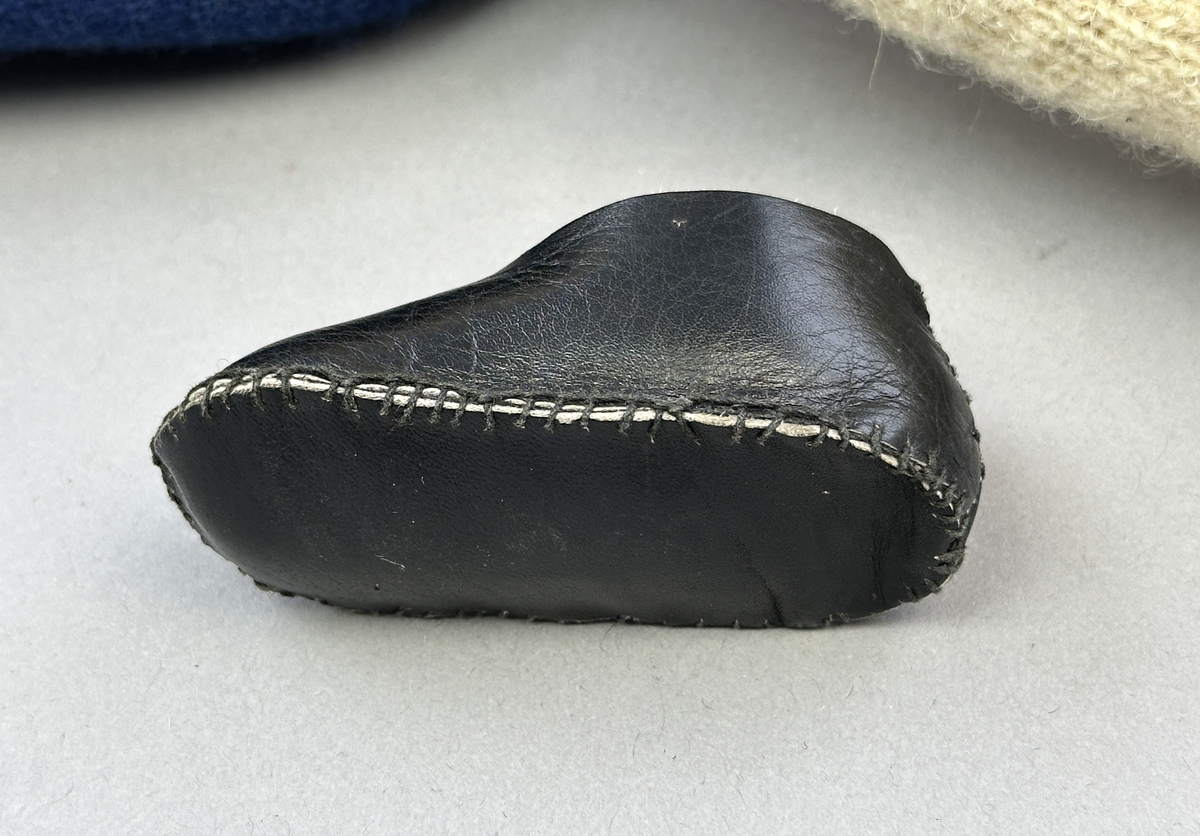 Docka klädd i kvinnlig sockendräkt från Ulleruds socken i Värmland. Kroppen är handsydd i linnetyg och stoppad med textilt material. Huvud och händer är av lergods. Kläder handsydda av handvävda tyger förutom skjorta, underkjol och halskläde, som är maskinvävt. Skjorta, broderad med myrgång runt sprund, har halsspjäll, halslinning och handlinning. Halsklädet, med tryck i gult, rosa och beige, hålls ihop av en sölja i nysilver med graverat mönster. Kjol sydd med lagda veck runtom, utom under förkläde, vars linning består av ett bomullsband. Förkläde, vävt i tuskaft och munkabälte, har lagda veck vid midja och bomullsband i rips till knytband. Livstycket är vändsytt/fodrat med ett rutigt bomullstyg och knäpps med 6 hyskar & hakar. Ullstrumporna är handstickade i slätstickning med en kant upptill i 2-2 resår. Huvudet är prytt med en vit linnehätta kantad med en knypplad linnespets. Dockans fötter bär svarta skinnskor.