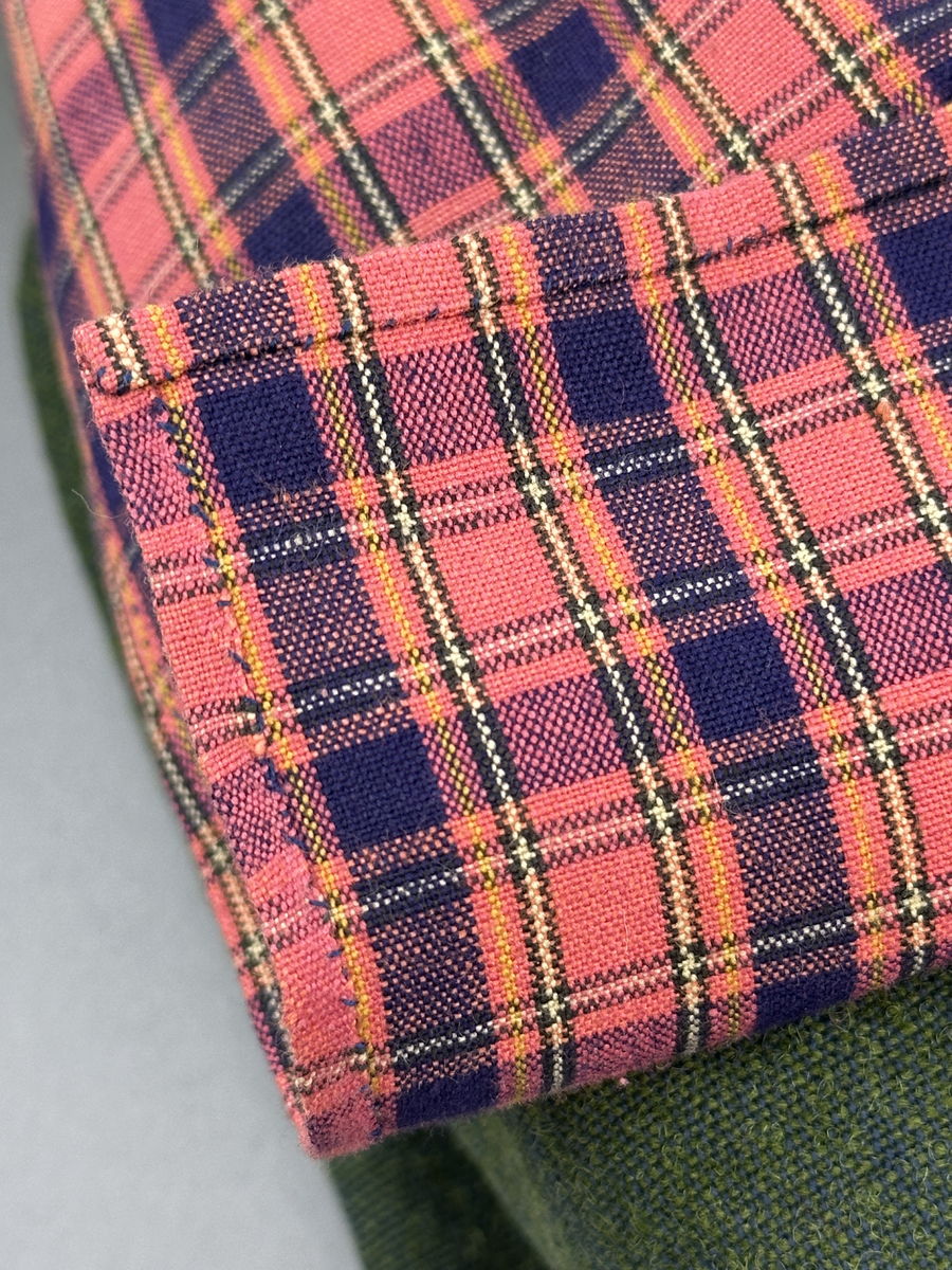 Docka klädd i kvinnlig sockendräkt från Dalby socken i Värmland. Kroppen är handsydd i linnetyg och stoppad med textilt material. Huvud och händer är av lergods. Kläder handsydda av handvävda tyger förutom skjorta, underkjol och halskläde, som är maskinvävt. Skjortan består av halsspjäll, krage och handlinning med stripade veck runt  krage och manschett. Skjortan är broderad med rutsöm vid sprund, krage, axelsöm och handlinning. Knytband bestående av trefläta (i rött och vitt) och tofsar (i rött, vitt och blått) pryder krage och manschett. Livkjol sydd med lagda veck runtom, utom under förkläde, har hals- och ärmhål kantad med passpoaler. Tyg till livkjol är vävt med bomullsvarp och ullinslag. Livet på livkjolen är vändsytt/fodrat med ett linnetyg och knäpps med 3 hyskar & hakar. Livkjolen är också dekorerad med en tre-fläta av rött ullgarn i nederkant. Även förklädet har lagda veck vid midja fastsydda mot en linning av bomullsband. Ullstrumporna är handstickade i slätstickning med en kant upptill i 2-2 resår samt en rad med avigmaskor, som "söm"-dekor på baksida ben. Huvudet är prytt med en vit linnehätta kantad med en knypplad linnespets samt ett broderi i blått och rött. Dockans fötter bär svarta skinnskor.

