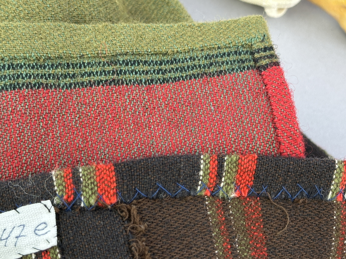 Docka klädd i kvinnlig sockendräkt från Fryksdals härad i Värmland. Kroppen är handsydd i linnetyg och stoppad med textilt material. Huvud och händer är av lergods. Kläder handsydda av handvävda tyger förutom skjorta, underkjol och halskläde, som är maskinvävt. Halskläde är broderat med tambursöm i gult, rosa, vinrött och grönt i 3 olika nyanser. Skjortan har halsspjäll, halslinning och stripade veck runt halskrage. Livkjol sydd med lagda veck runtom, utom under förkläde. Tyget till livkjol och förkläde är vävt med bomullsvarp och ullinslag. Även förklädet har lagda veck vid midja fastsydda mot en linning av bomullsband. Livet på livkjolen är vändsytt/fodrat med ett linnetyg och knäpps med 5 hyskar & hakar. Ullstrumporna är handstickade i slätstickning med en kant upptill i 2-2 resår samt en rad med avigmaskor, som "söm"-dekor på baksida ben.