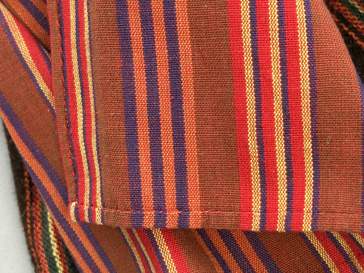 Docka klädd i kvinnlig sockendräkt från Sunne socken i Värmland. Kroppen är handsydd i linnetyg och stoppad med textilt material. Huvud och händer är av lergods. Kläder handsydda av handvävda tyger förutom skjorta, underkjol och halskläde, som är maskinvävt. Skjorta, broderad med stopphålsömsbroderi i vitt lingarn längs sprund mitt fram, har stripade veck runt krage och manschett. Halskläde, broderad med tambursöm i vitt moulinegarn, hålls ihop av en sölja i nysilver med graverat mönster. Yllekjol är rynkad upptill, utom under förkläde, vars linning och skoningsband består av ett bomullsband. Förklädet har lagda veck vid midja fastsydda mot en linning av bomullsband. Livstycket med sköld i ylletyg, är vändsytt/fodrat med ett mönstrat bomullstyg och knäpps med 5 hyskar & hakar samt har 2 små tennknappar fastsydda på utsidan. Ullstrumporna är handstickade i slätstickning med en kant upptill i 2-2 resår. Huvudet är prytt med en vit linnehätta kantad med en knypplad linnespets. Dockans fötter bär svarta skinnskor.