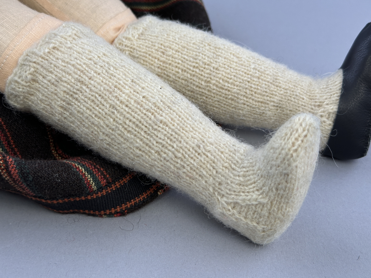Docka klädd i kvinnlig sockendräkt från Sunne socken i Värmland. Kroppen är handsydd i linnetyg och stoppad med textilt material. Huvud och händer är av lergods. Kläder handsydda av handvävda tyger förutom skjorta, underkjol och halskläde, som är maskinvävt. Skjorta, broderad med stopphålsömsbroderi i vitt lingarn längs sprund mitt fram, har stripade veck runt krage och manschett. Halskläde, broderad med tambursöm i vitt moulinegarn, hålls ihop av en sölja i nysilver med graverat mönster. Yllekjol är rynkad upptill, utom under förkläde, vars linning och skoningsband består av ett bomullsband. Förklädet har lagda veck vid midja fastsydda mot en linning av bomullsband. Livstycket med sköld i ylletyg, är vändsytt/fodrat med ett mönstrat bomullstyg och knäpps med 5 hyskar & hakar samt har 2 små tennknappar fastsydda på utsidan. Ullstrumporna är handstickade i slätstickning med en kant upptill i 2-2 resår. Huvudet är prytt med en vit linnehätta kantad med en knypplad linnespets. Dockans fötter bär svarta skinnskor.