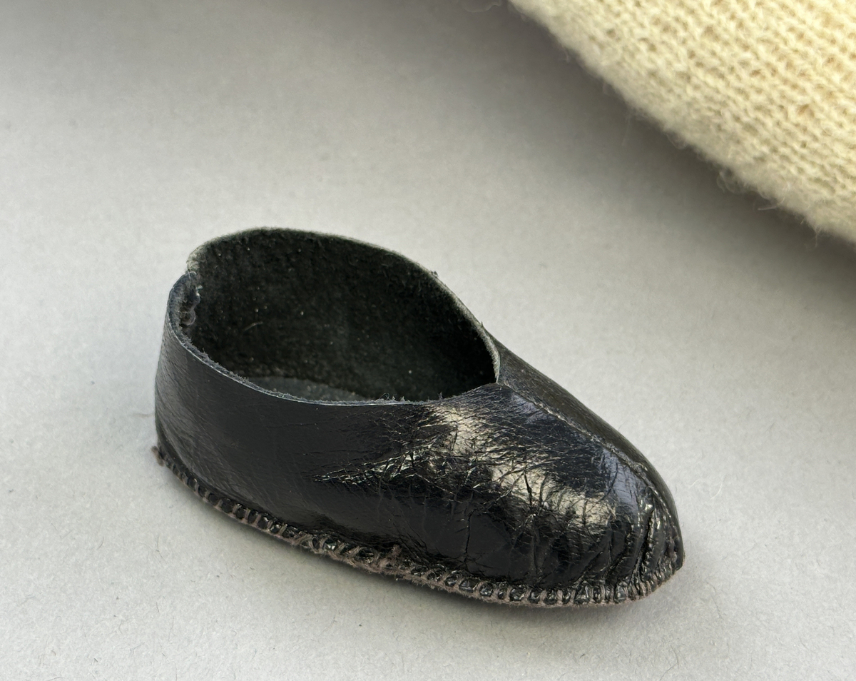 Docka klädd i kvinnlig sockendräkt från Sunne socken i Värmland. Kroppen är handsydd i linnetyg och stoppad med textilt material. Huvud och händer är av lergods. Kläder handsydda av handvävda tyger förutom skjorta, underkjol och halskläde, som är maskinvävt. Skjorta, broderad med stopphålsömsbroderi i vitt lingarn längs sprund mitt fram, har stripade veck runt krage och manschett. Halskläde, broderad med tambursöm i vitt moulinegarn, hålls ihop av en sölja i nysilver med graverat mönster. Yllekjol är rynkad upptill, utom under förkläde, vars linning och skoningsband består av ett bomullsband. Förklädet har lagda veck vid midja fastsydda mot en linning av bomullsband. Livstycket med sköld i ylletyg, är vändsytt/fodrat med ett mönstrat bomullstyg och knäpps med 5 hyskar & hakar samt har 2 små tennknappar fastsydda på utsidan. Ullstrumporna är handstickade i slätstickning med en kant upptill i 2-2 resår. Huvudet är prytt med en vit linnehätta kantad med en knypplad linnespets. Dockans fötter bär svarta skinnskor.