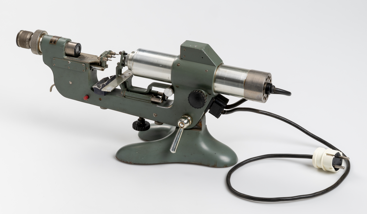 Vertometer, optiskt instrument för analys av linser, tillverkad av gjutjärn, stål, aluminium och glas. Grönlackerad. Dyna för märkfärg saknas.
Såld av Uppsala Optiska Industri AB.