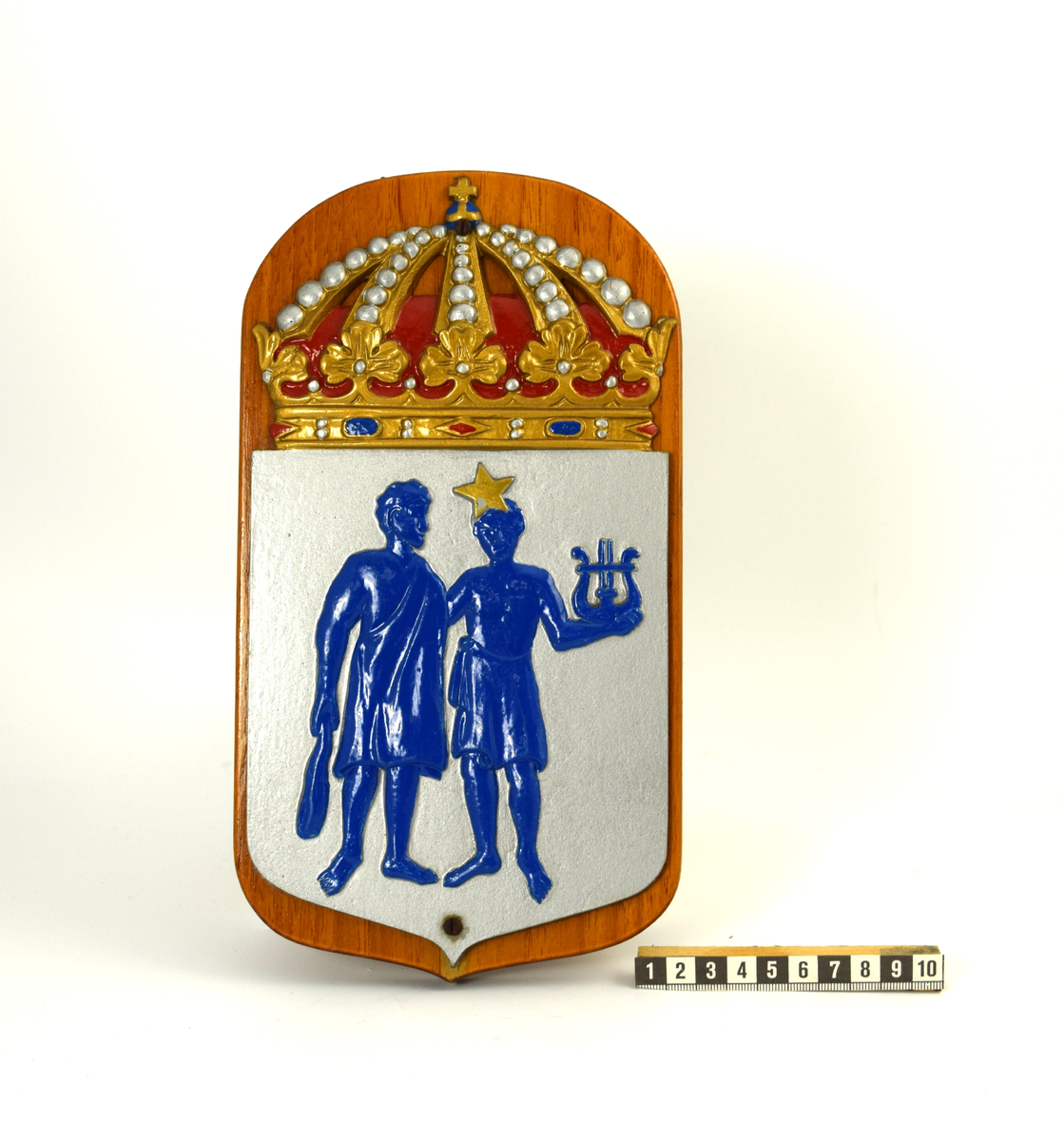 Vapensköld bestående av en metallplatta fastskruvad på en lackerad träplatta. Bilden på vapnet föreställer de två grekiska gudarna Pollux och Castor i blå färg mot en silvrig bakgrund. Pollux håller en klubba i höger hand och Castor håller ett spelinstrument i form av en lyra i sin vänstra hand. På Castors panna ses en femuddig stjärna i guldig färg. Vapnet är krönt med en kungakrona i färgerna guld, silver, rött och blått.