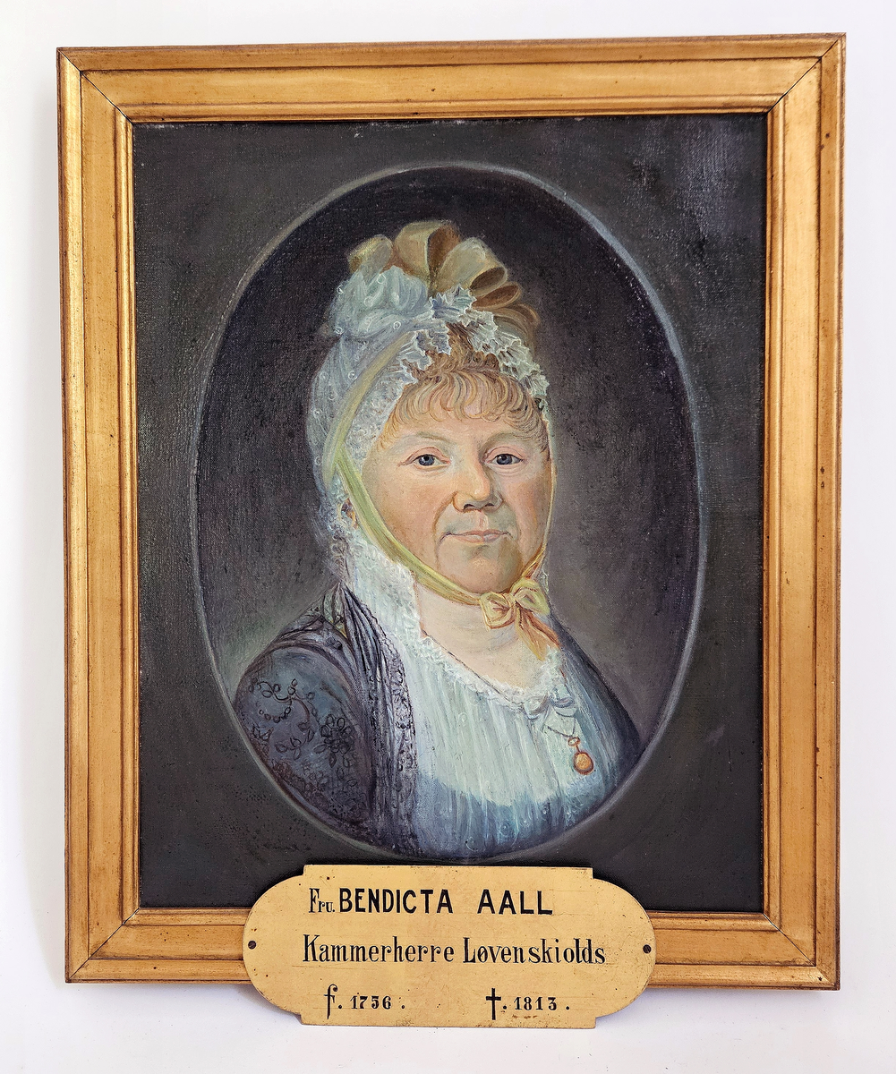 Fra protokollen: Fru Bendicta Aall Kammerherre Løvenskiolds f. 1756 d. 1813 (sign. paa namneplate). Oljemaala kopi av pastel paa Fossum, portræt i avlangrundt felt av kvende med kvit kappe paa hovudet, en face til h. (R. Berge)