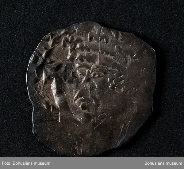 Silvermynt, England Henry II (1154-89), penny 1158-80. North 956-70 var; SCBI 12 Oxford 301 ff, 'Cross and crosslets'-typ. 
Vikt: 1,385 g.

Bro kastal i Bro socken, Lysekils kommun byggdes under 1110-talet. Kastalen bestod av ett kraftigt fristående torn, uppfört uppe på en kulle och var en tidig typ av borganläggning. Från kastalen hade man milsvid utsikt över den omgivande trakten.
Kastalens grund mäter en fyrkant om 8,7 x 8,4 meter. Invändigt har funnits valvslaget tak och halvmeterbreda inre gångar. Tornets ursprungliga höjd bedöms till 10 meter.
Fynden från arkeologiska undersökningar på 1960- och 1970-talen visar att kastalen varit i bruk från 1100-talet fram till början av 1400-talet. 
Tre mynt daterar kastalen; en engelsk silverpenny från andra halvan av 1100-talet, ett mynt från antingen kung Sverres (1176 -1202) eller sonen  Håkon Håkonssons regering samt ett fragmentariskt mynt från perioden 1160-1205, av okänt ursprung. 
Mycket i fyndmaterialet ger en koppling till samhällets övre skikt, bl.a. en guldring, en piksporre, en nöt (del till ett armborst) och en stjärntrissa till en sporre. 
Bland benfynden finns rester av duvhök som kan ha varit dresserad för jakt. 
Till vapenfynden hör en stridsyxa av järn från 1100-talet och fyra pilspetsar. 
En del bruksföremål som brynen, en kläppkrok som användes vid havsfiske och en ljusterudd tyder på att borgen varit bebodd åtminstone tidvis (se Pettersson, J. 1987).