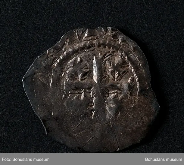 Silvermynt, England Henry II (1154-89), penny 1158-80. North 956-70 var; SCBI 12 Oxford 301 ff, 'Cross and crosslets'-typ. 
Vikt: 1,385 g.

Bro kastal i Bro socken, Lysekils kommun byggdes under 1110-talet. Kastalen bestod av ett kraftigt fristående torn, uppfört uppe på en kulle och var en tidig typ av borganläggning. Från kastalen hade man milsvid utsikt över den omgivande trakten.
Kastalens grund mäter en fyrkant om 8,7 x 8,4 meter. Invändigt har funnits valvslaget tak och halvmeterbreda inre gångar. Tornets ursprungliga höjd bedöms till 10 meter.
Fynden från arkeologiska undersökningar på 1960- och 1970-talen visar att kastalen varit i bruk från 1100-talet fram till början av 1400-talet. 
Tre mynt daterar kastalen; en engelsk silverpenny från andra halvan av 1100-talet, ett mynt från antingen kung Sverres (1176 -1202) eller sonen  Håkon Håkonssons regering samt ett fragmentariskt mynt från perioden 1160-1205, av okänt ursprung. 
Mycket i fyndmaterialet ger en koppling till samhällets övre skikt, bl.a. en guldring, en piksporre, en nöt (del till ett armborst) och en stjärntrissa till en sporre. 
Bland benfynden finns rester av duvhök som kan ha varit dresserad för jakt. 
Till vapenfynden hör en stridsyxa av järn från 1100-talet och fyra pilspetsar. 
En del bruksföremål som brynen, en kläppkrok som användes vid havsfiske och en ljusterudd tyder på att borgen varit bebodd åtminstone tidvis (se Pettersson, J. 1987).