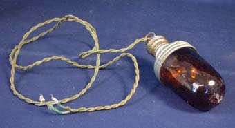 Cylinderformad kupa av brunt glas fastskruvad i hylsa av metall som i sin tur består av två ihopskruvade metallyhyllsor och en krans av vitt porslin mellan dem. Inuti metallhylsan finns lampans elektriska ledningar. Från toppen av metallhylsan går två elektriska kablar klädda med textil och ihoptvinnade med varandra. Längd: ca 1600 mm. Innanför glaskupan och fastskruvad i metallhylsan finns en glödlampa.