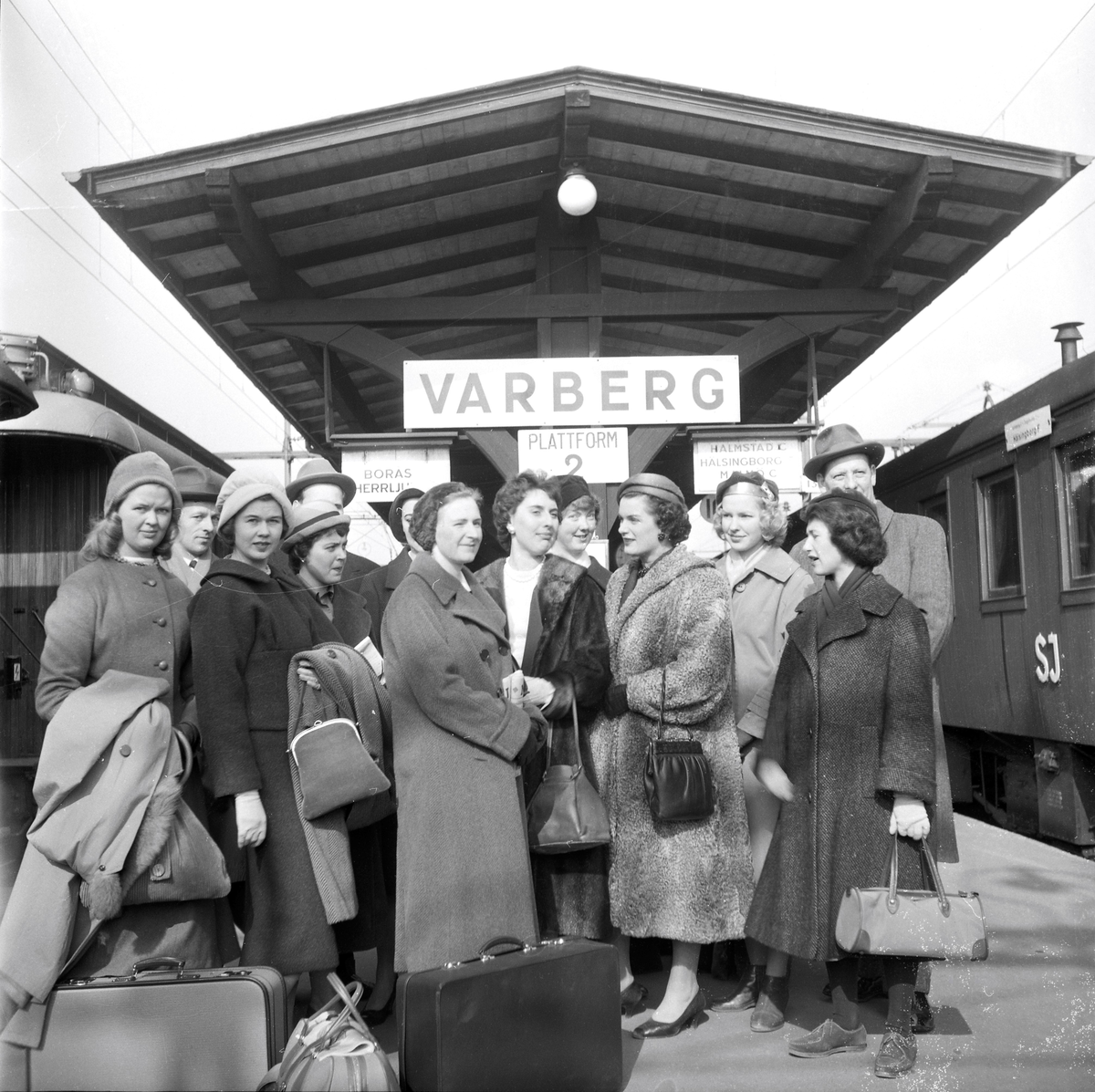 En grupp resklädda kvinnor på Varbergs tågperrong. De är elever från Textilhögskolan i Borås på väg till Berlin för att studera mode. Mannen längst till höger heter Birger Larsson och var rektor på skolan. Några av de övriga damerna är Birgit Eliasdotter (boende i Varberg 2004), Kerstin Karlström och Birgitta Eliasson.
Bild 2 visar två av kvinnorna skrattandes på perrongen.