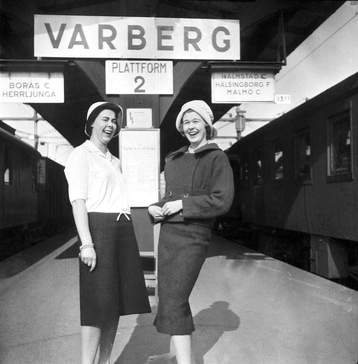 En grupp resklädda kvinnor på Varbergs tågperrong. De är elever från Textilhögskolan i Borås på väg till Berlin för att studera mode. Mannen längst till höger heter Birger Larsson och var rektor på skolan. Några av de övriga damerna är Birgit Eliasdotter (boende i Varberg 2004), Kerstin Karlström och Birgitta Eliasson.
Bild 2 visar två av kvinnorna skrattandes på perrongen.