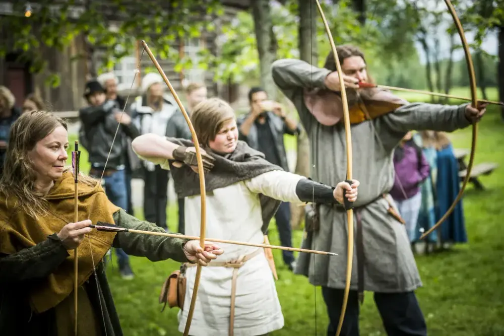 Tre vikingkledde mennesker med buer. Publikum i bakgrunnen.