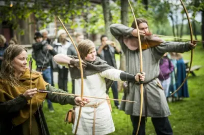 Tre vikingkledde mennesker med buer. Publikum i bakgrunnen.