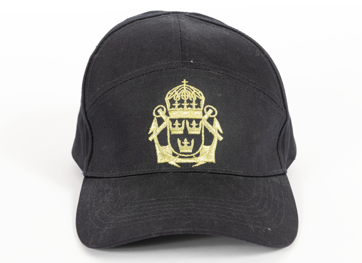 Mörkblå skärmmössa, keps. Framtill emblem i guldfärg: korslagda ankare med tre kronor i krönt sköld.