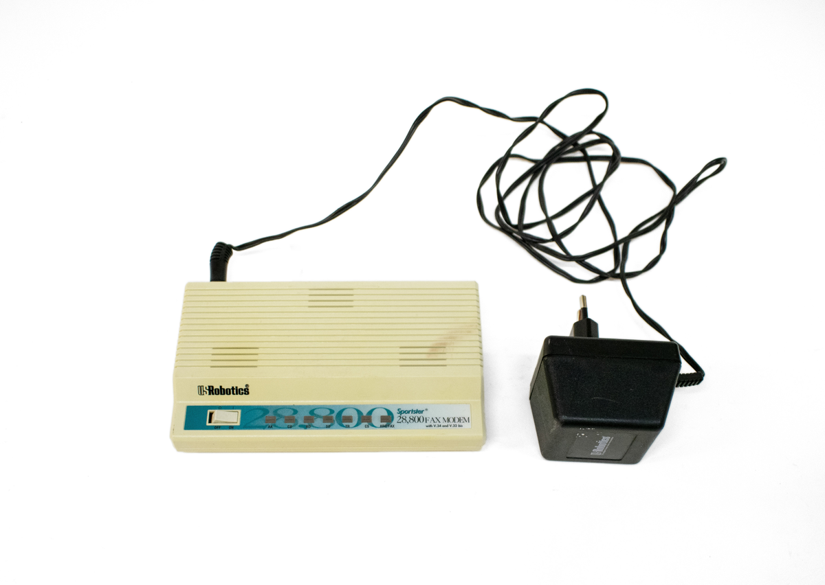 Faksmodem med strømadapter. Hvitbeige (gulnet) boks med luftekanaler på toppen. Av -og på-knapp på venstre framdel, samt ulike lampeindikatorer.
Modell: Sportster 28,800 FAX MODEM with V,34 and V,32 bis.