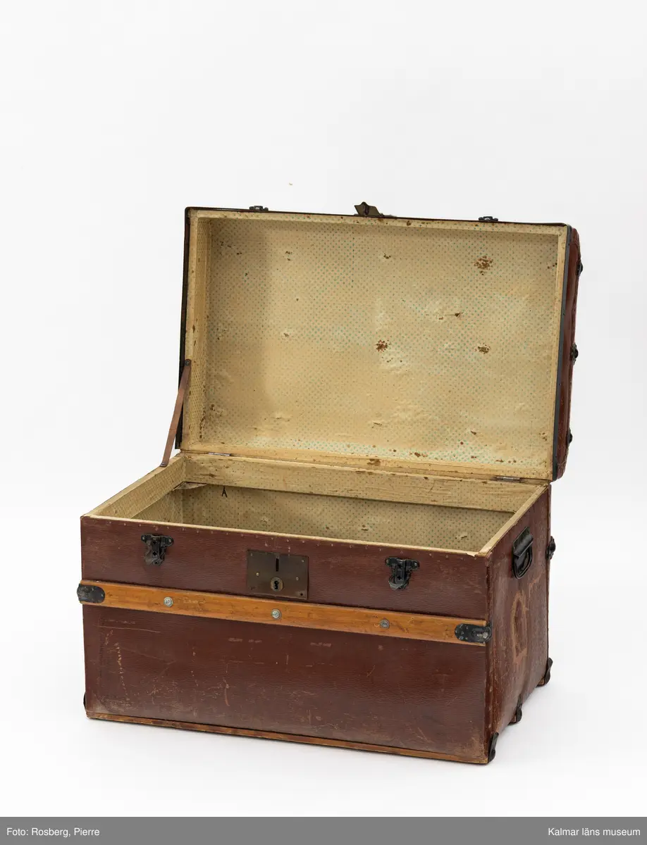 KLM 32017. Koffert, reskoffert, trä, metall, textil, läder, färg, Brun, rektangulär koffert med ett handtag av metall på varje gavel. På fronten ett nyckellås samt två låsspännen av mässing. Ribbor av trä med mässingsbeslag runt kofferten som skydd/stötdämpning. Inuti klädd med vit papp med grönt mönster. På locket handskrift i svart: Curt Stoopendaal Stockholm.